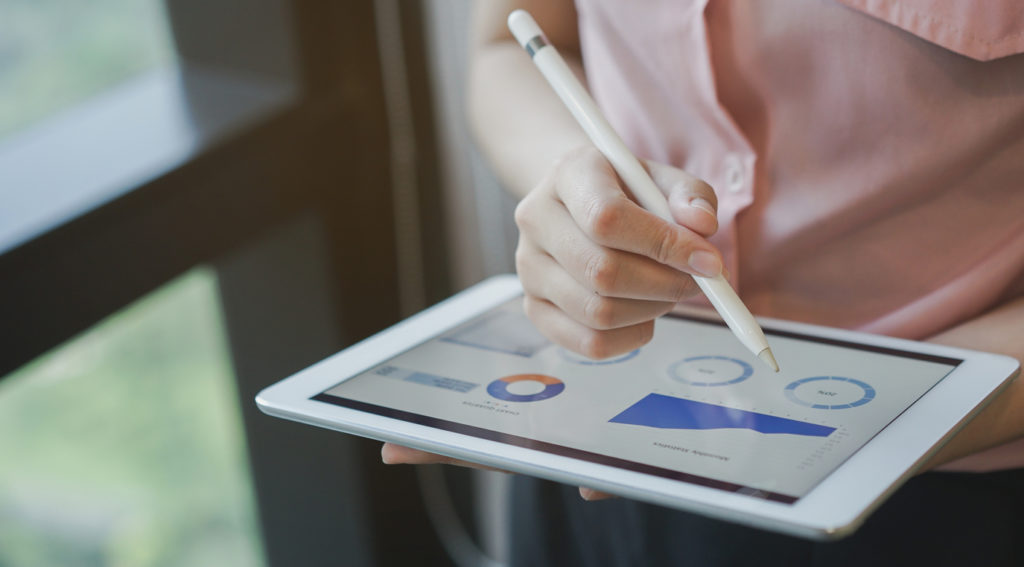 A woman using a tablet and stylus to review KPIs on a dashboard for her medical practice.