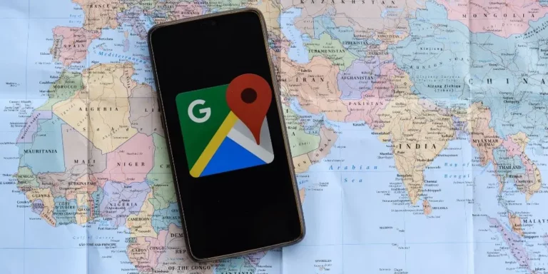Smartphone with Google Maps app icon laying on top of a paper map